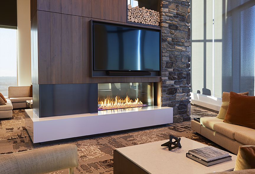 Modern living room with a sleek double-sided fireplace incorporating a tv above, surrounded by stone and wood details. large windows provide natural light, complementing the cozy seating area.