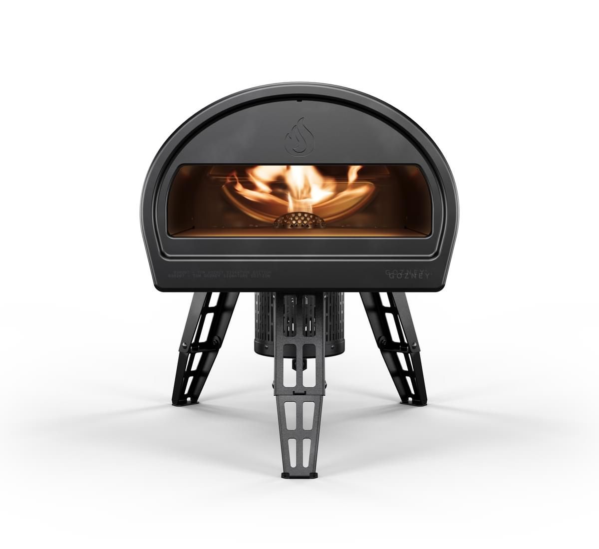 Portable, black Tom Gozney Signature Edition Roccbox Pizza Oven on a stand, with visible fire inside, showcasing Gozney brand logo on the front.