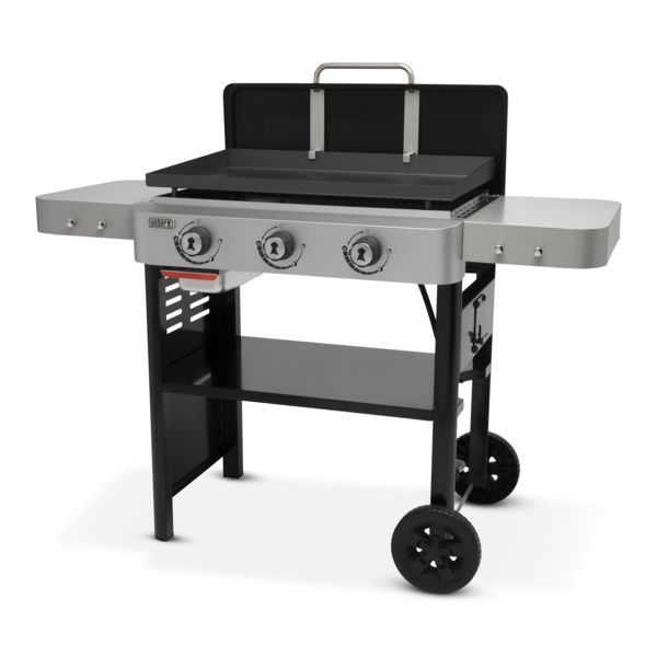 A modern, three-burner Weber Griddle 28" with an open lid, featuring side shelves and a lower storage shelf, mounted on wheels for mobility, isolated on a white background.