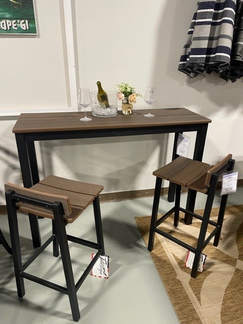 A modern dining setup with a narrow dark wood Bazza table and two matching stools, topped with a bottle of wine, two glasses, and a small floral arrangement in a brightly lit room.