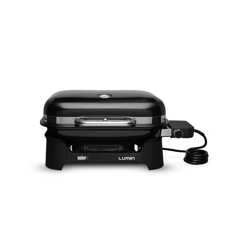 A black weber lumin electric grill with a closed lid, positioned on a stand with visible controls and a connected power cord.