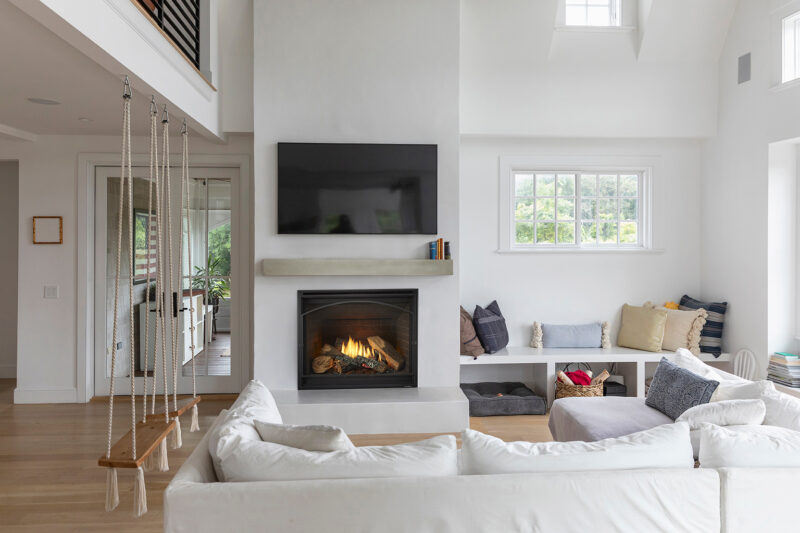 A cozy, modern living room featuring a white sectional sofa, a Heat & Glo 6K/8K Series Gas Fireplace, and a swing hanging from the ceiling, with bright natural light coming through