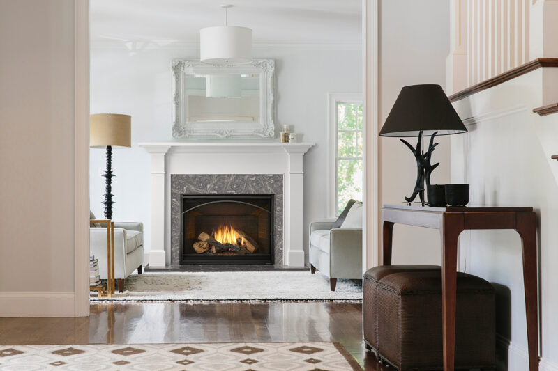 A cozy living room featuring a lit fireplace with a white mantel, flanked by stylish armchairs and elegant decor, including a unique black lamp on a side table.