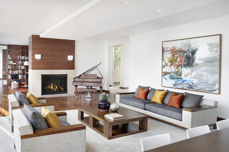 Elegant living room with a Heatilator Caliber Gas Fireplace, grand piano, and a large abstract painting. Features sleek furniture with colorful cushions, a bookcase, and natural lighting.