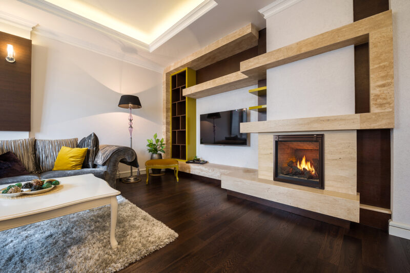 Modern living room with wooden shelves, a Heat & Glo 6K/8K Series Gas Fireplace, a plush sofa, and a white coffee table on a shaggy rug. Warm lighting and