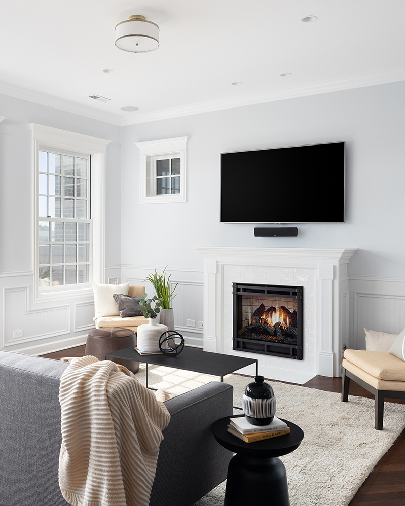 Modern living room with a muted color palette featuring a SimpliFire Inception Electric Fireplace, wall-mounted TV, a beige sofa, gray armchairs, and minimalistic decor. Bright natural light floods