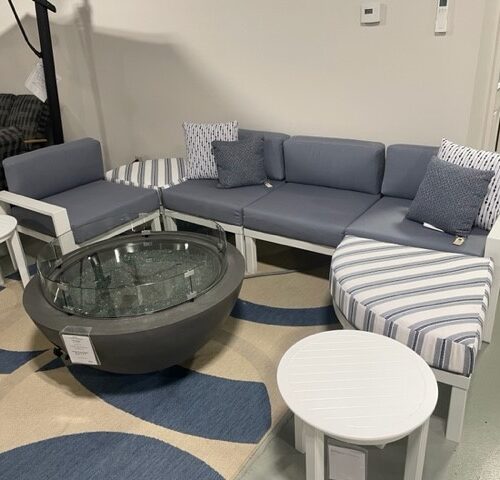 A modern living area featuring a Larssen sectional sofa with striped cushions, complemented by white round side tables and a round glass-top coffee table on a blue and gray area rug.