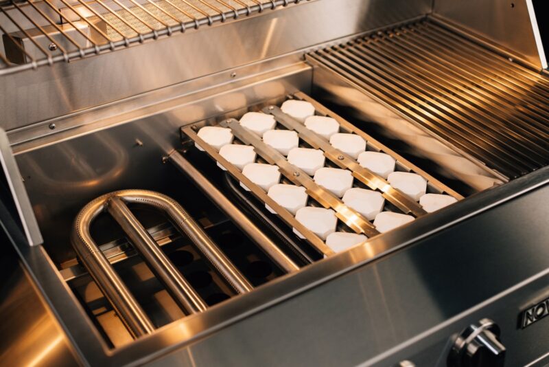 Inside of a commercial kitchen oven with twin trays of bread rolls baking, illuminated by the oven light.