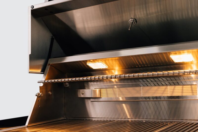 A stainless steel commercial kitchen hood with twin bright internal lighting over a grill, emphasizing a clean, modern culinary environment.