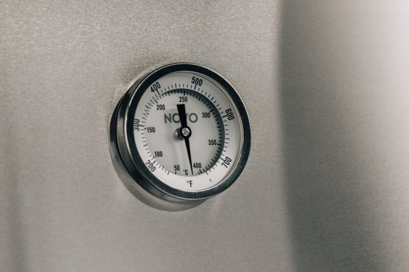A close-up view of a twin, round, stainless steel dial thermometer mounted on a gray metal surface, displaying a temperature around 250 degrees Fahrenheit.