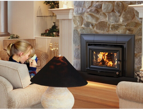 A cozy living room with a woman sitting on a couch, drinking from a mug, by a lit fireplace enclosed in a stone wall. a table lamp and ornate decor accentuate the warm, inviting atmosphere.
