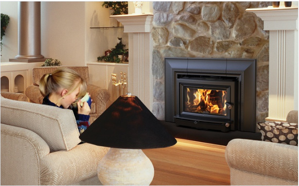 A cozy living room with a woman sitting on a couch, drinking from a mug, by a lit fireplace enclosed in a stone wall. a table lamp and ornate decor accentuate the warm, inviting atmosphere.