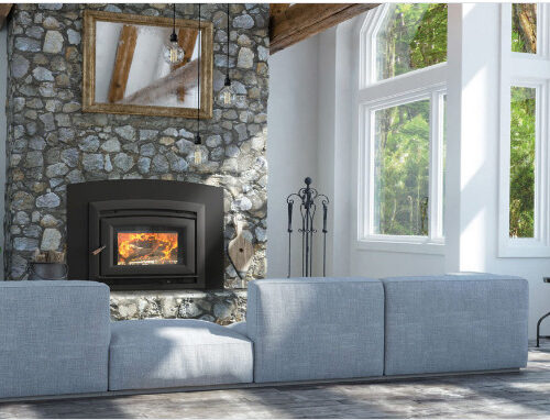 A cozy room with a stone fireplace burning wood, framed by a large gray sectional couch and tall windows offering plenty of natural light. a plant and unique lamp add charm to the space.
