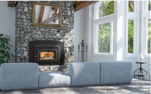 A cozy room with a stone fireplace burning wood, framed by a large gray sectional couch and tall windows offering plenty of natural light. a plant and unique lamp add charm to the space.