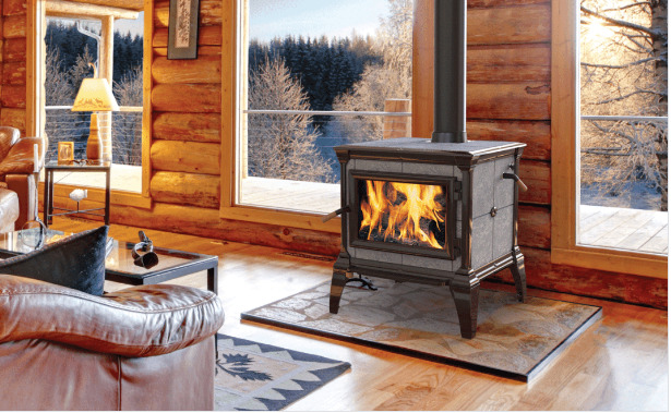 A cozy cabin interior with a lit fireplace, wooded walls, and windows showing a snowy landscape outside. plush seating and warm lighting add to the inviting atmosphere.