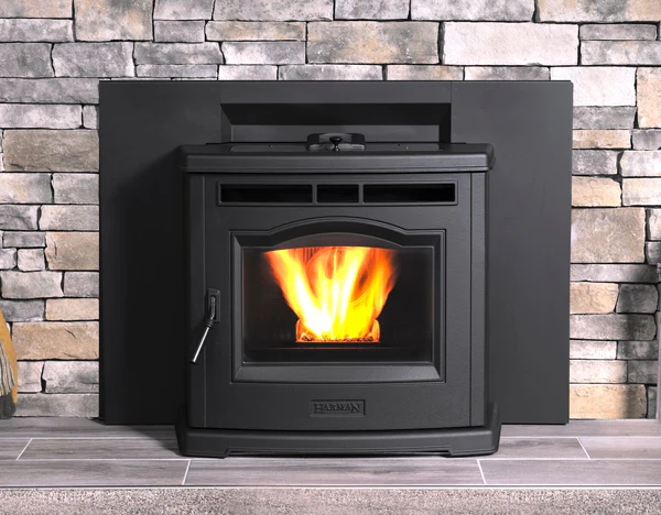 A modern black wood-burning stove with a visible fire through a glass door, set against a stone wall backdrop.