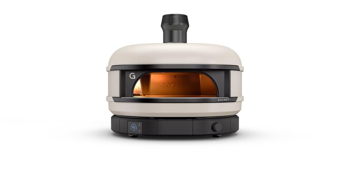 A modern, portable pizza oven with a sleek design, featuring a front glass door and a visible flame inside, set against a plain white background.