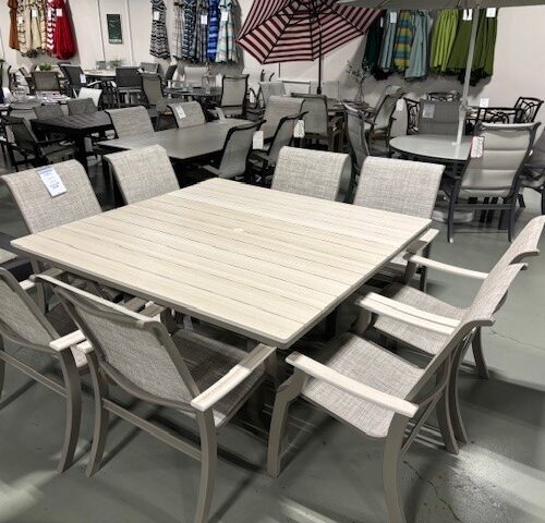 A furniture showroom displaying various outdoor dining sets including St. Catherine Sling chairs and tables in different styles and materials, arranged neatly on a grey floor.