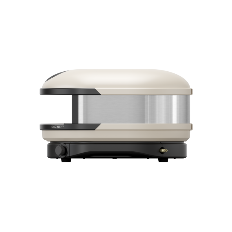A modern, compact pizza oven with a sleek beige and silver design, featuring a visible brand name on the front.