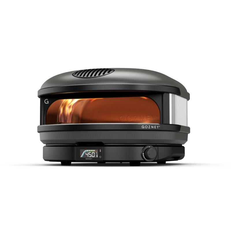 A modern, portable gozney pizza oven with a digital temperature display, showing 450°f. the oven is designed with a black exterior, glass front, and visible flames inside.