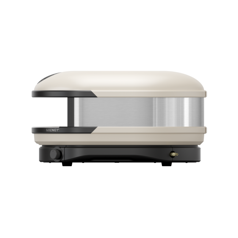 A modern, pizza oven with a stylish beige and silver design, featuring a front handle and visible grill lines on the plate.