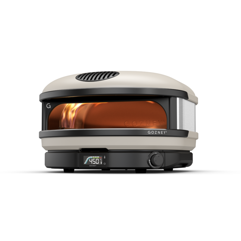 A modern gozney portable outdoor pizza oven with a digital temperature display showing 450° f. the oven has visible flames inside, with a sleek beige and gray design.