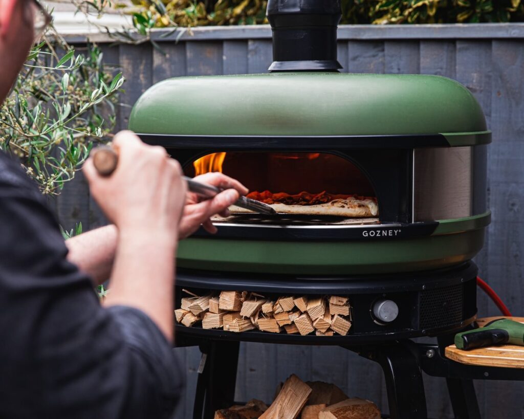  A man removing a pizza from a sleek olive dome Gozney pizza oven