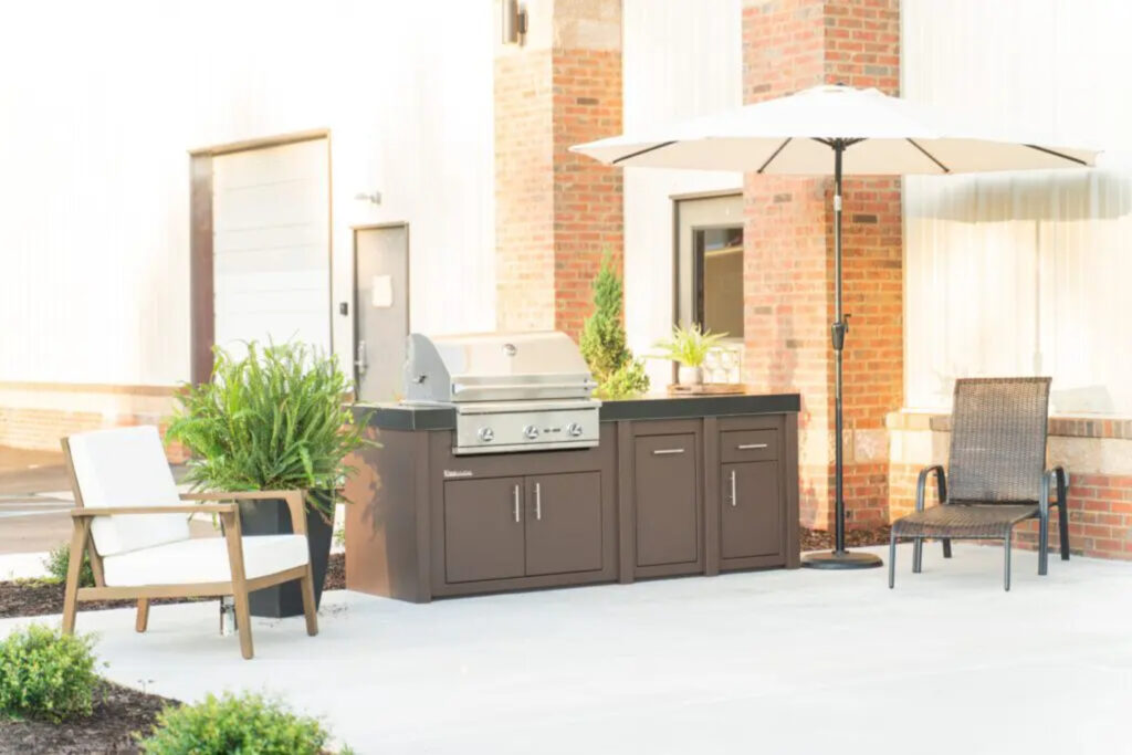 An outdoor kitchen with dark wood, black countertops, and stainless-steel appliances, surrounded by outdoor furniture and plants