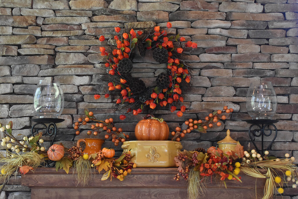 Fireplace mantel with a stone wall background, decorated with fall decor and glass objects